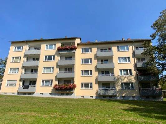 Rückansicht zweier verbundener mehrstöckigen Wohngebäuden mit Balkonen umgeben von einer grünen Außenanlage