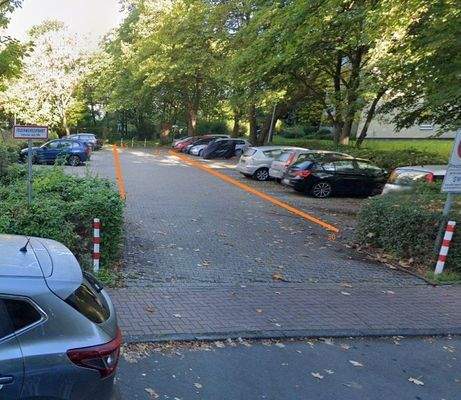 Parkplatz Ansicht mit Beschriftung der Stellplatznummern umgeben von Bäumen und Sträuchern. 