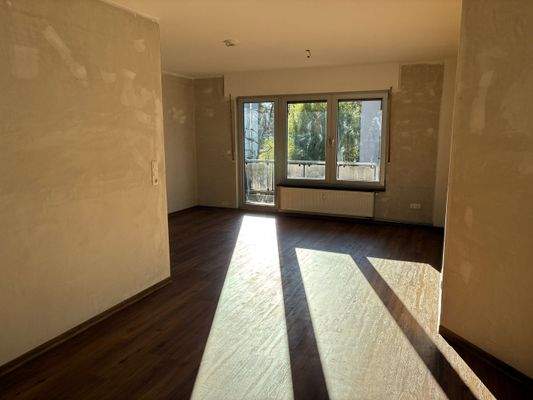 Ess- und Wohnbereich mit untapezierten Wänden, braunem Vinyl-Designboden und Zugang zum Balkon