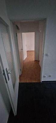 Flur mit PVC-Bodenbelag in Holzoptik und tapezierten Wänden.