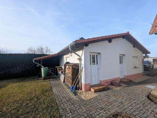 Nebengebäude mit Doppelgarage und Abstellraum sowie überdachtem Unterstand für Müllbehälter, daneben Lagerung Kaminholz