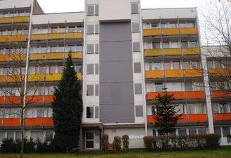 Vorderansicht eines 6 geschossigen Wohnhauses mit Eingang und Bepflanzung