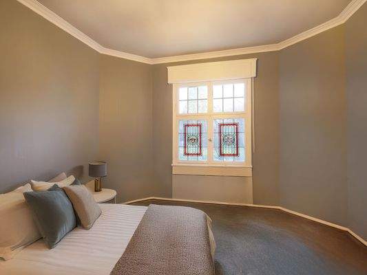 Geräumiges Schlafzimmer mit großen Fenstern und historischem Charakter (Möblierung KI-generiert)