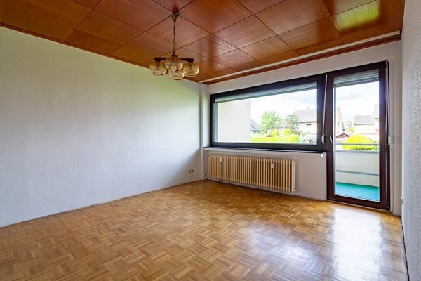 Das Wohnzimmer mit Parkettboden und Zugang zum Balkon lädt zum Wohlfühlen ein