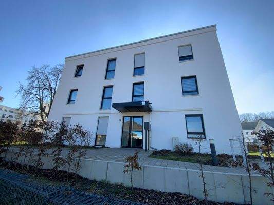 Vorderansicht eines mehrstöckigen weißen Wohngebäudes mit Fenstern und Eingangsbereich