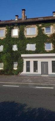 Außenansicht mit Gewerbeeinheit im EG und öffentlichen Parkplätzen davor