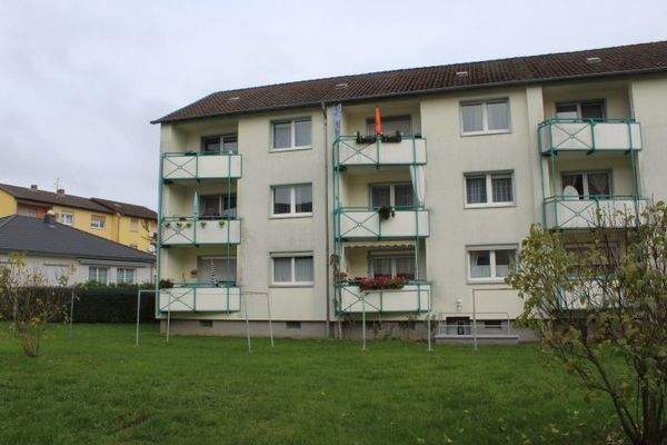 Blick auf das dreitsöckige Mehrfamilienhaus mit Rasen und Balkonen an jeder Wohnung  