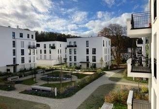 Außenanlage des Neubaus mit modernen weißen Wohngebäuden, mit einem zentralen Weg, der die Wohnhäuser miteinander verbindet.