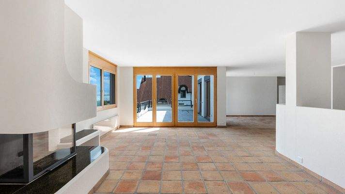 Open-plan Living mit Cheminée, grossen Fensterfronten und Zugang zur sonnigen Terrasse 