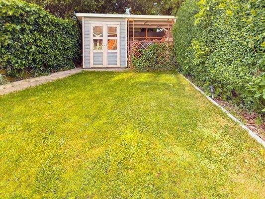 Blickgeschützte Rasenfläche mit Gartenhäuschen und Unterstand zur Kaminholzlagerung