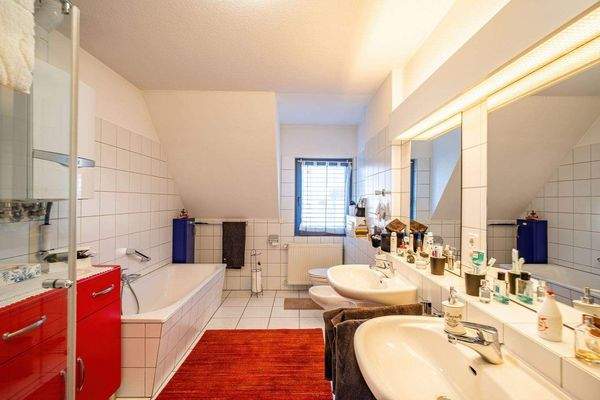 Das Bad ist weiß gefliest und mit Badewanne, Glasd