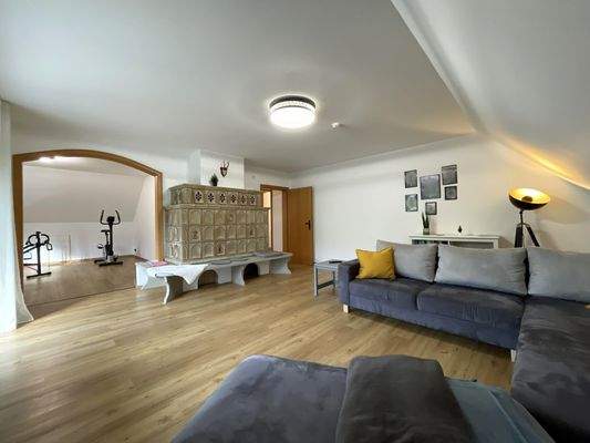 Dachgeschoss: Wohnzimmer mit gemütlichem Kachelofen und weiter in den Fitnessraum