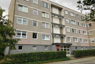 Außenansicht des mehrstöckigen Wohngebäudes umgeben von Bäumen und Hecken