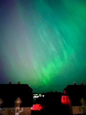 Polarlichter über den reetgedeckten Nachbarhäusern und dem Bootssteg in der Marina, Ansicht II