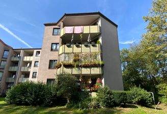 Rückansicht mehrerer aneinanderhängender hellen Mehrfamilienhäuser mit Balkonen, umgeben von einer grünen Rasenfläche hinter dem Haus.