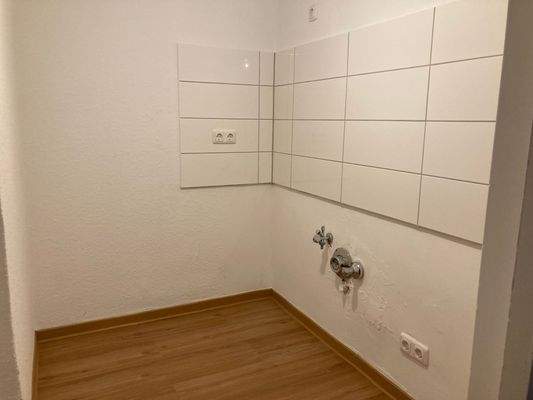 Küche mit weißem Fliesenspiegel und Fußboden in Holzoptik.