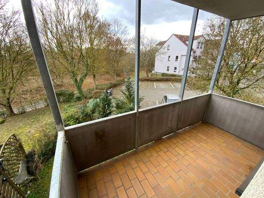 Balkon mit braunrotem Steinboden mit Blick in die grüne Außenanlage mit Parkplatz.jpg