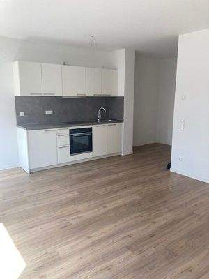 Einbauküche mit weißen Fronten und dunkler Rückwand im Wohnzimmer integriert