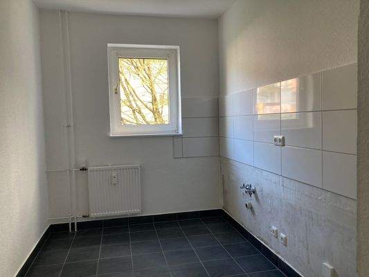 Küche mit schwarzen Bodenfliesen, weißem Fliesenspiegel und Fenster.