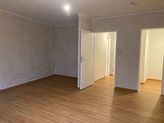 Wohn- und Schlafzimmer mit weißen Türen, tapetenlosen Wänden und Fußboden in Holzptik.