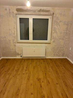 Wonzimmer. Decken weiß gestrichen. Wände tapezierfähig vorbereitet. Neuer brauner Vinylboden.