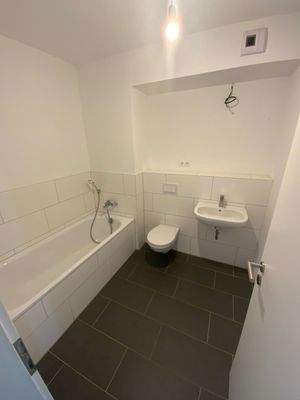 Badezimmer mit weißen Wand-WC, weißem Wandwaschbecken, Badewanne auf grauem Fliesenboden.JPG