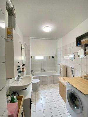 Badezimmer mit weißen Wand- und Bodenfliesen, weißem Wand-Waschbecken, Stand-WC und Badewanne und Mietereinrichtung.jpg