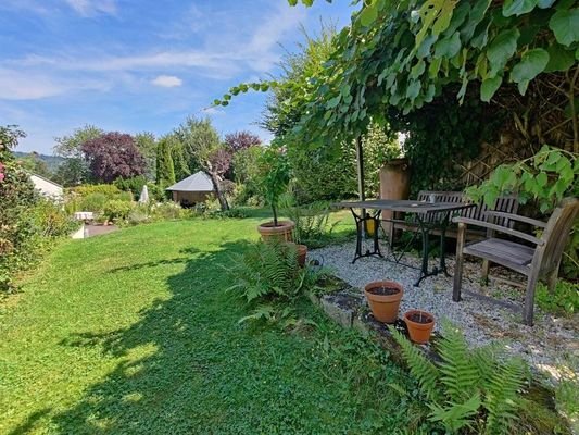 liebevoll angelegter Garten mit Holzhüttle und Sitzbereich im Schatten