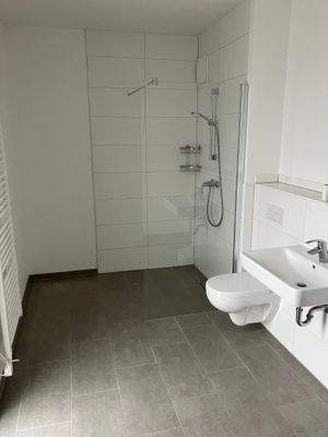 Beispielhaftes Bad mit Fenster, bodengleicher Dusche, wandhängendes WC, weißen Wandfliesen, dunkelgrauen Bodenfliesen