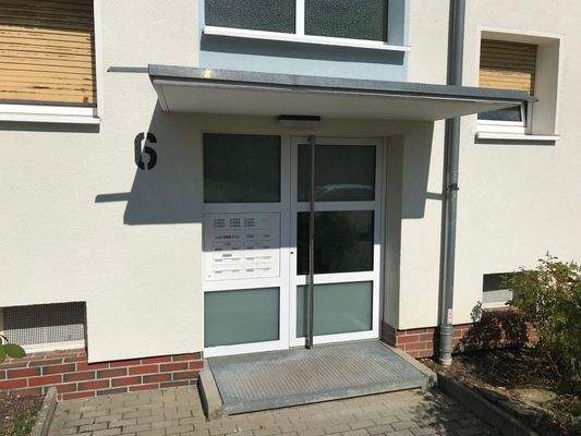 Hauseingang des mehrstöckigen Wohnhauses umgeben von Grünanlagen mit Bäumen