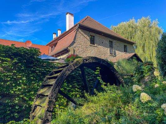 Ansicht Süd mit antikem Mühlenrad und Sonnenterrasse im Hintergrund